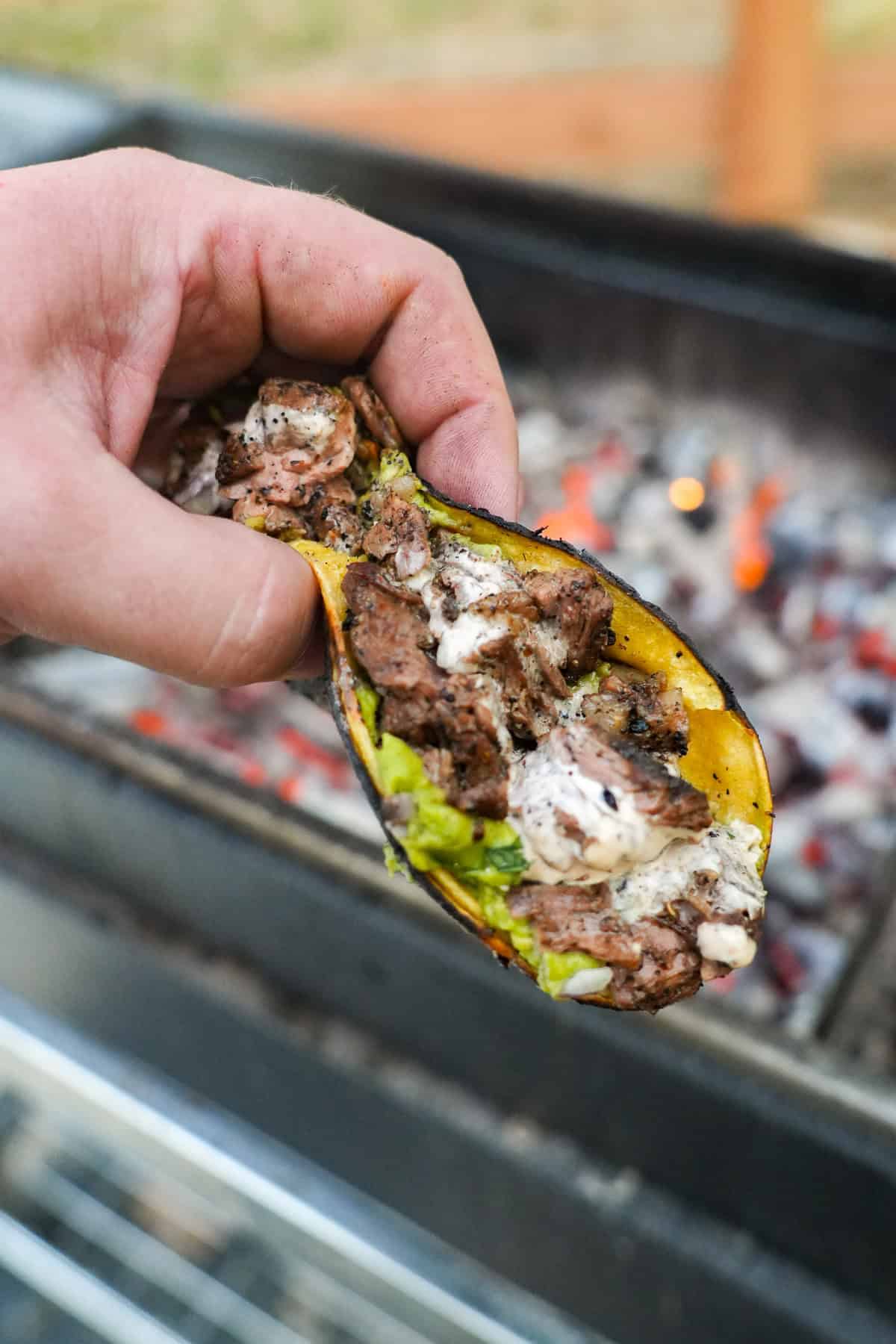 A close up of a single dirty steak taco with guacamole and chipotle sauce in front of the grill