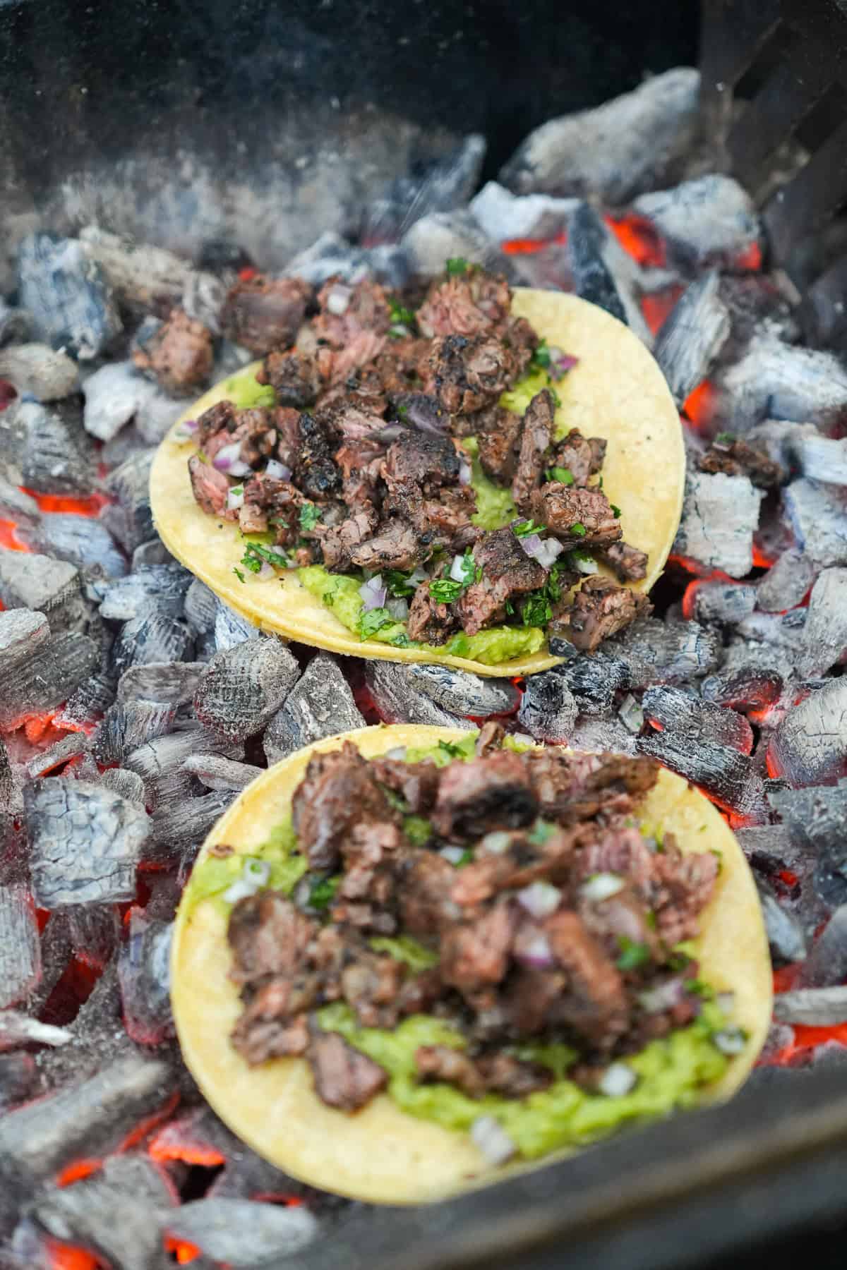 A close up of dirty steak tacos assembled and crisping up on top of the coals