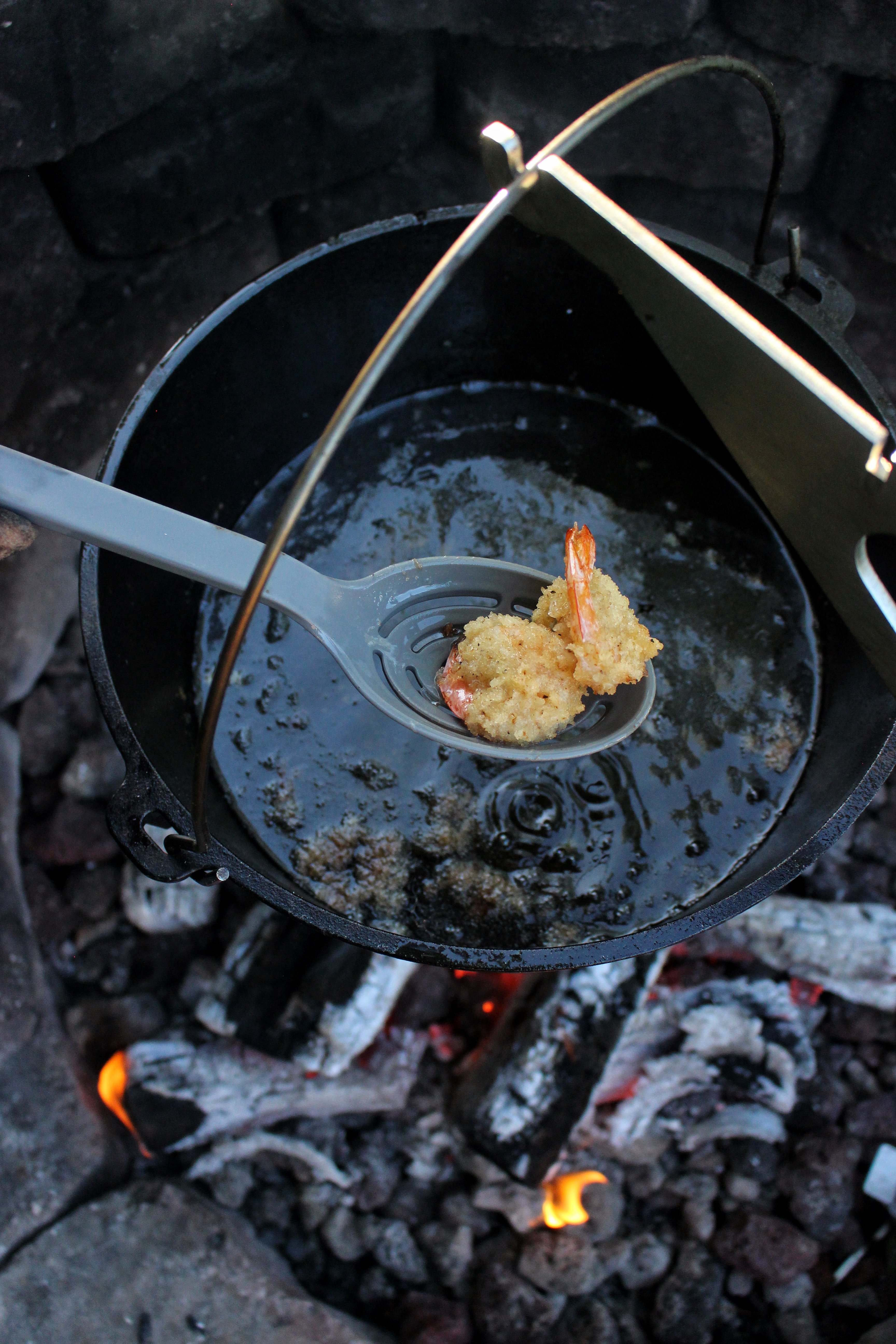 Pulling two fried shrimp from the dutch oven.