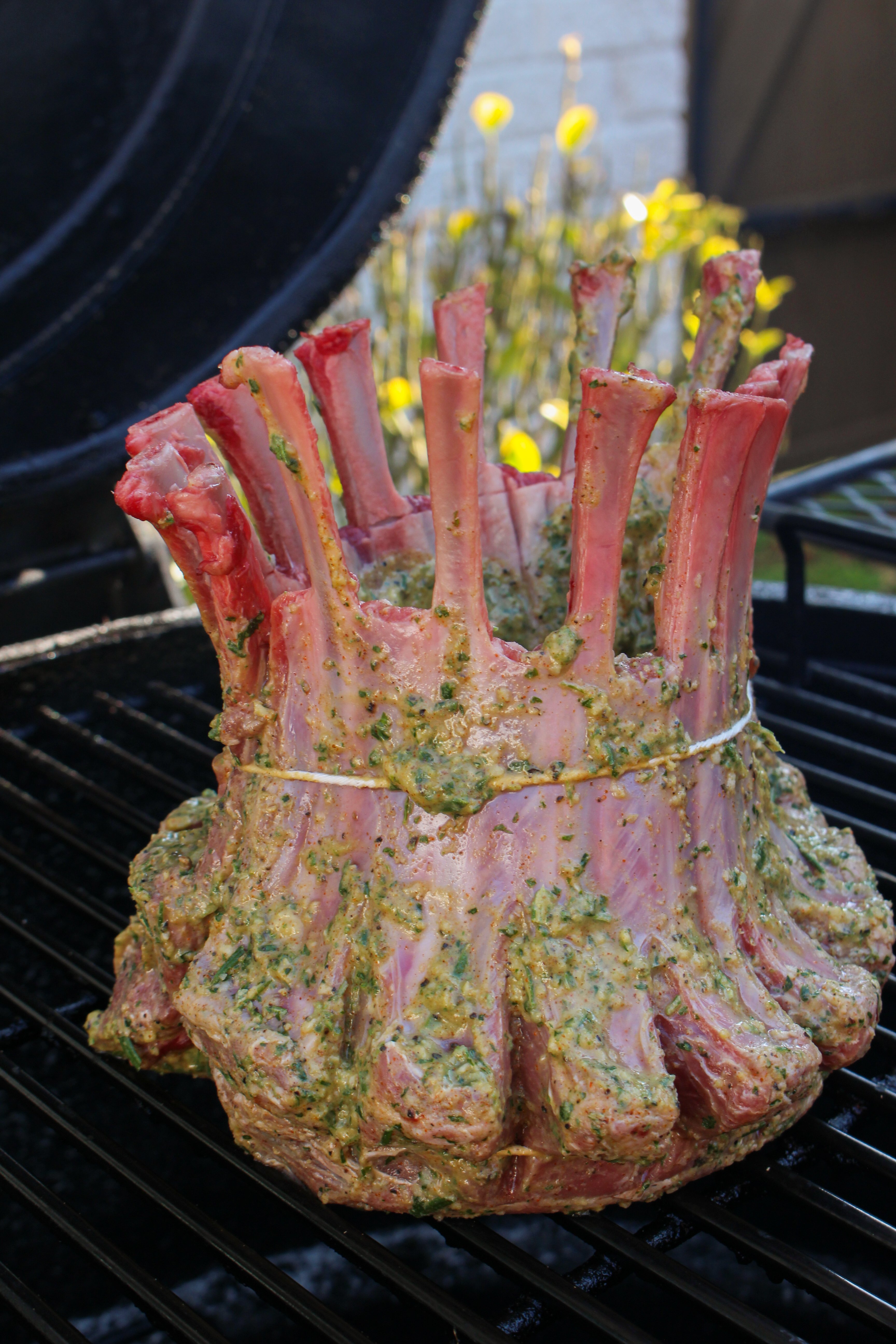 The raw lamb crown roast sitting seasoned on the smoker. 