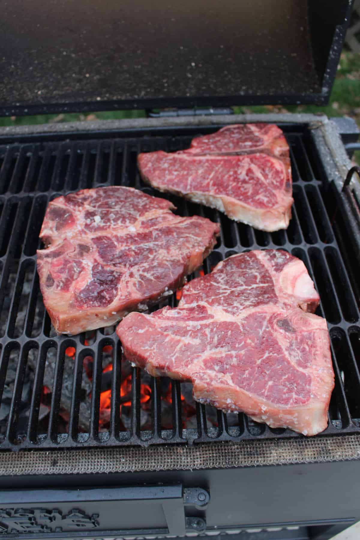 The raw steaks getting placed on the grill.