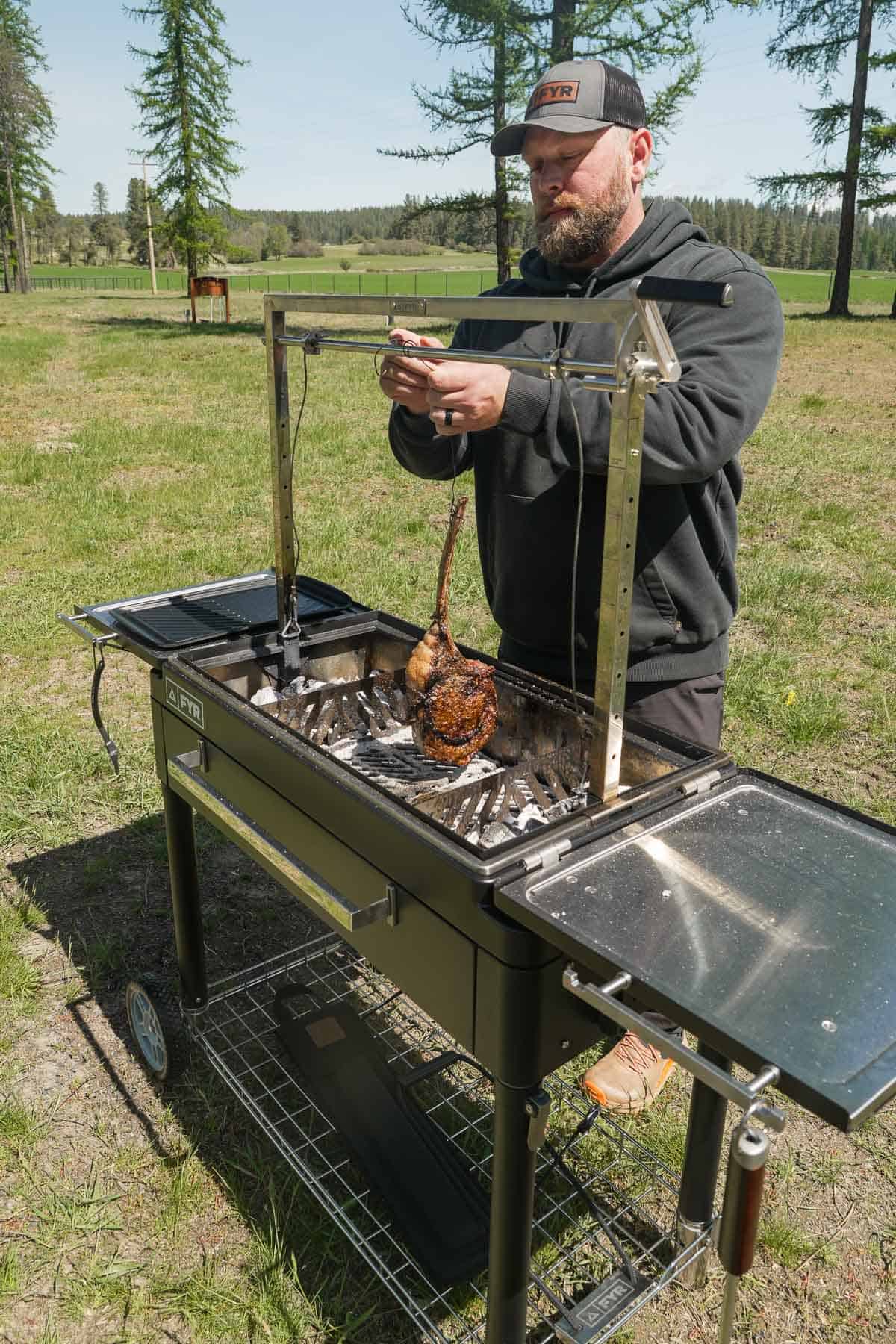 Derek Wolf pulling the hanging tomahawk steak off the FY Grill