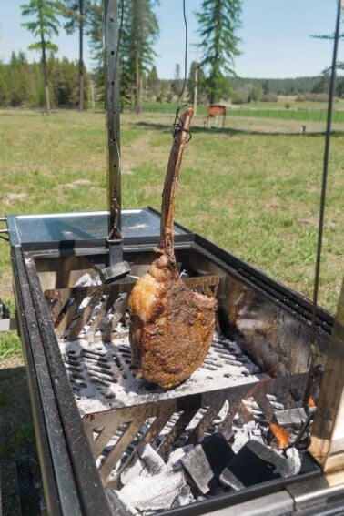 A hanging tomahawk steak over the three zone fire in the FYR Grill