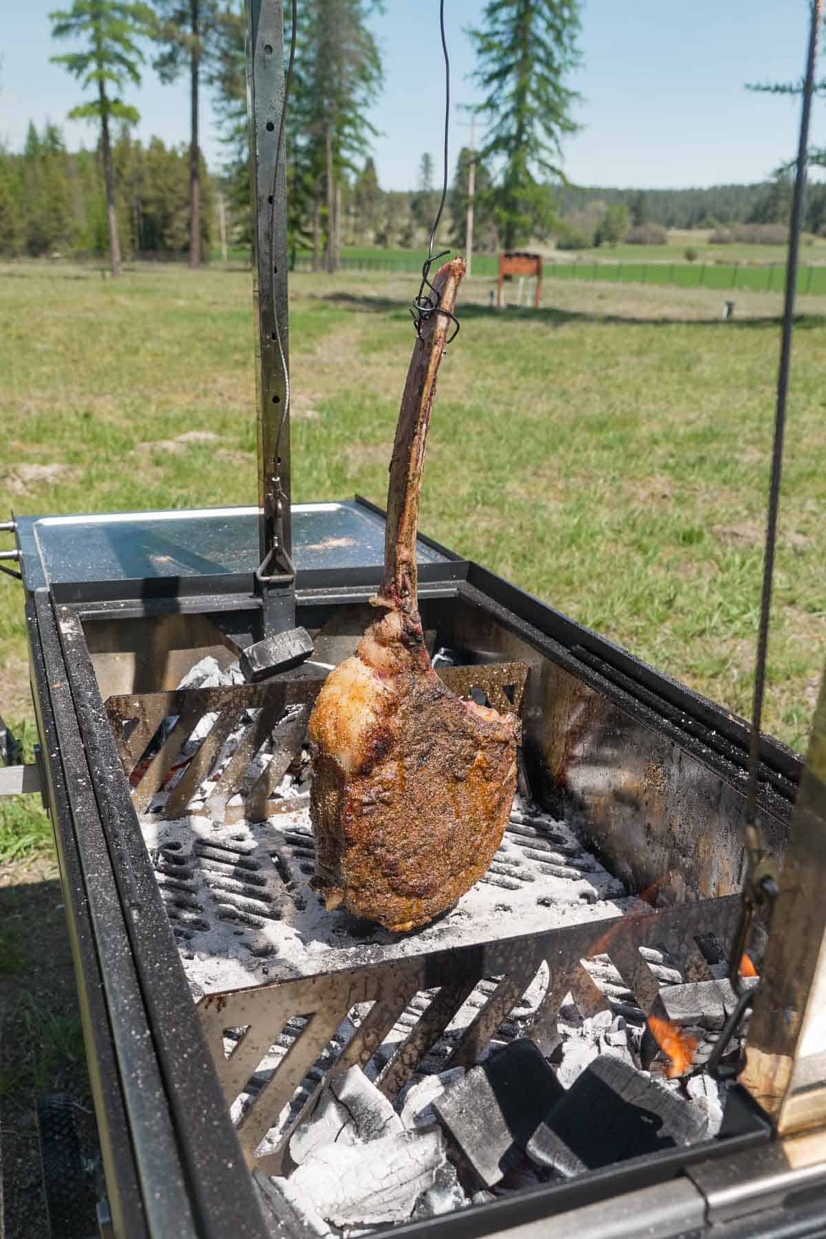 A hanging tomahawk steak over the three zone fire in the FYR Grill