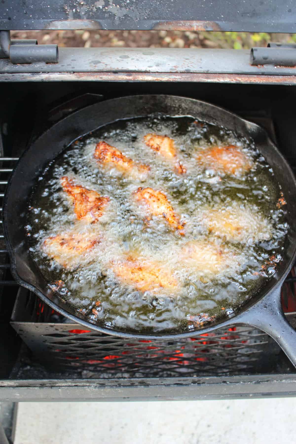 The frying chicken wings in the oil over the charcoal.