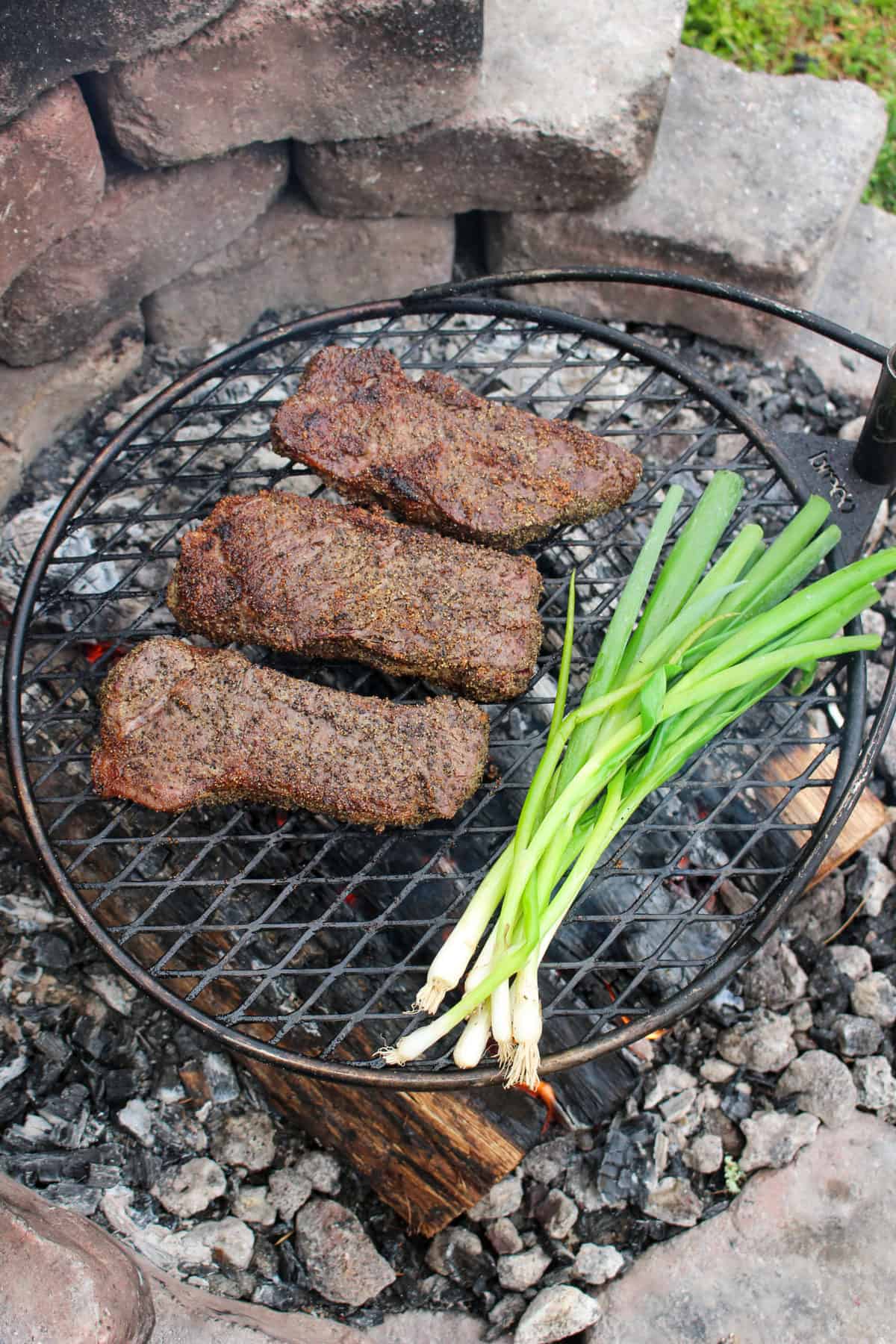 overhead shot of three steaks and a bunch of scallions on the grill
