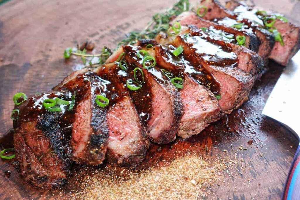 Steak topped with sauce sitting on the cutting board.