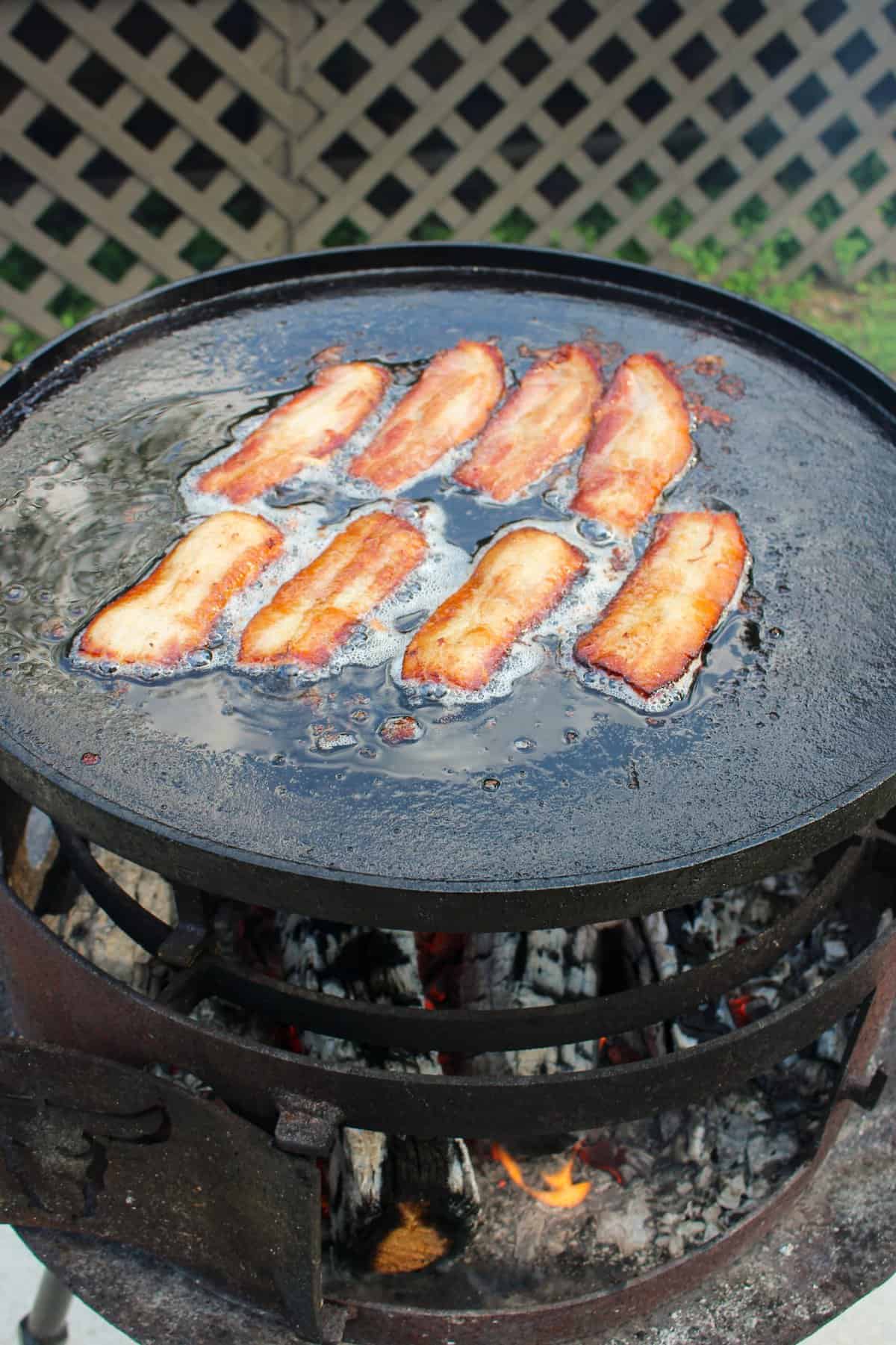 eight slices of bacon cooking on a large plancha