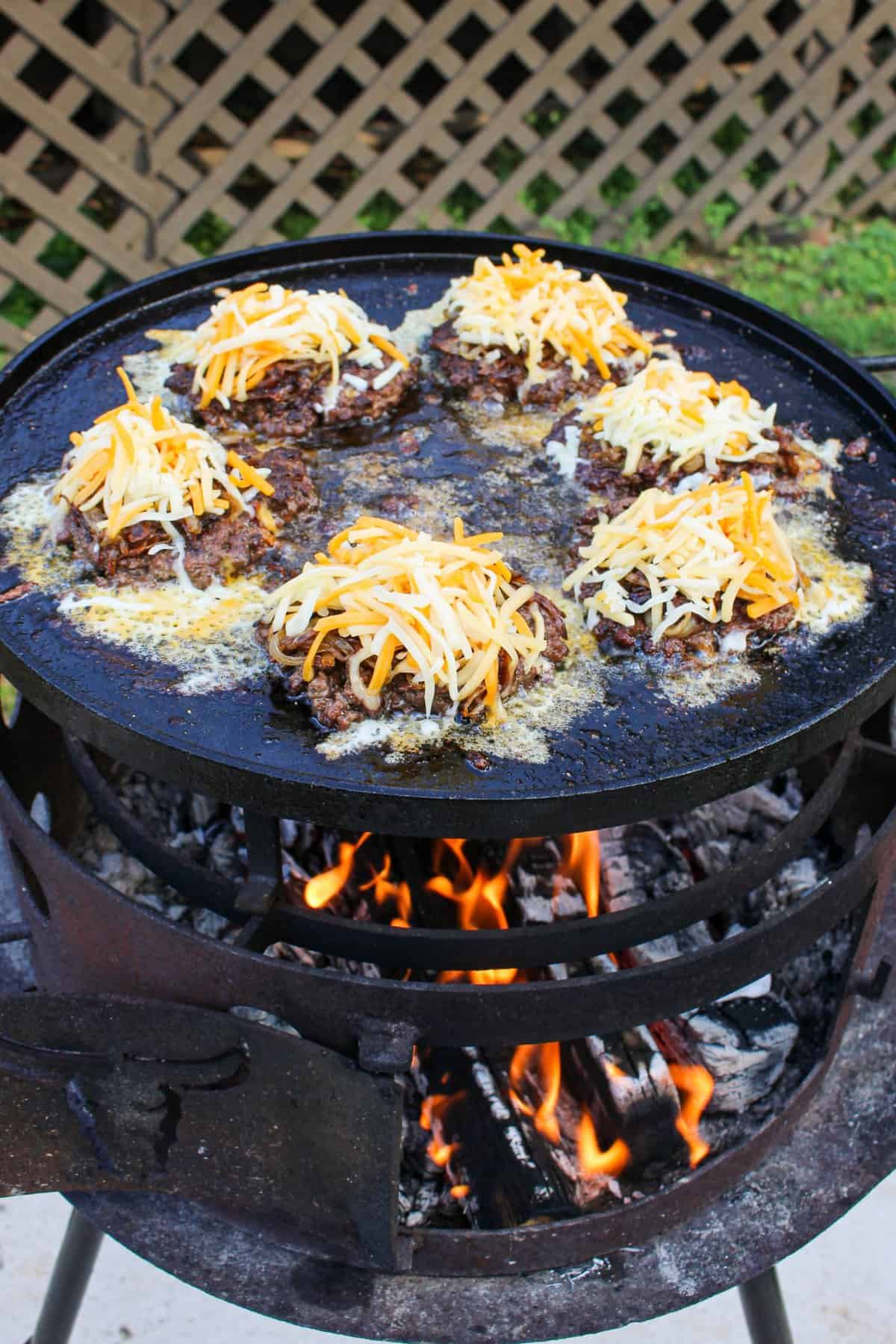 burger patties topped with cheese cooking on a large plancha