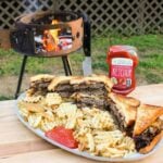 large platter on a table in front of a grill filled with cheesy patty melt sandwiches, fries, and ketchup