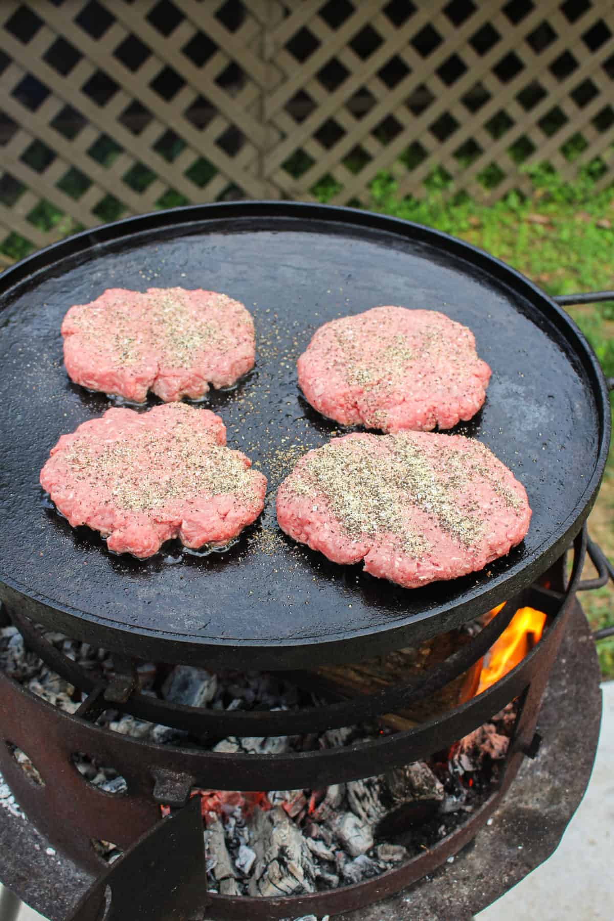 four burger patties being cooked on a large plancha