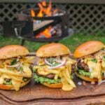 three California Burrito Style Burgers lined up on a cutting board in front of a grill