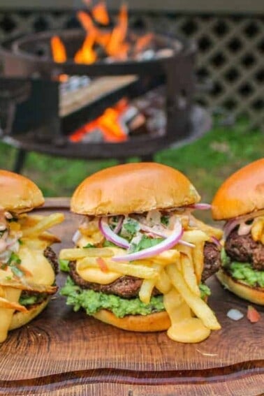 three California Burrito Style Burgers lined up on a cutting board in front of a grill