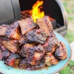 a pile of brisket burnt ends on a plate held next to a smoker