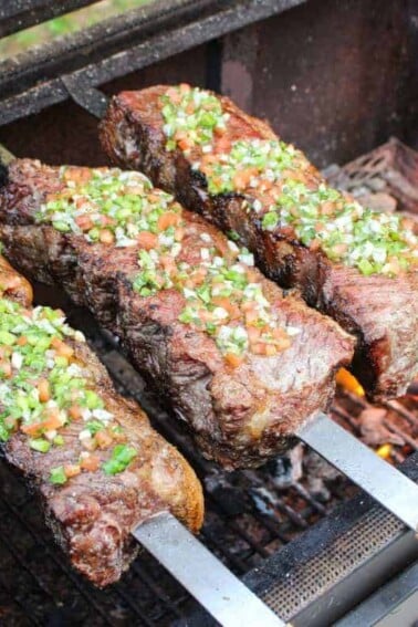 three strip steak skewers topped with salsa vinaigrette over a fire