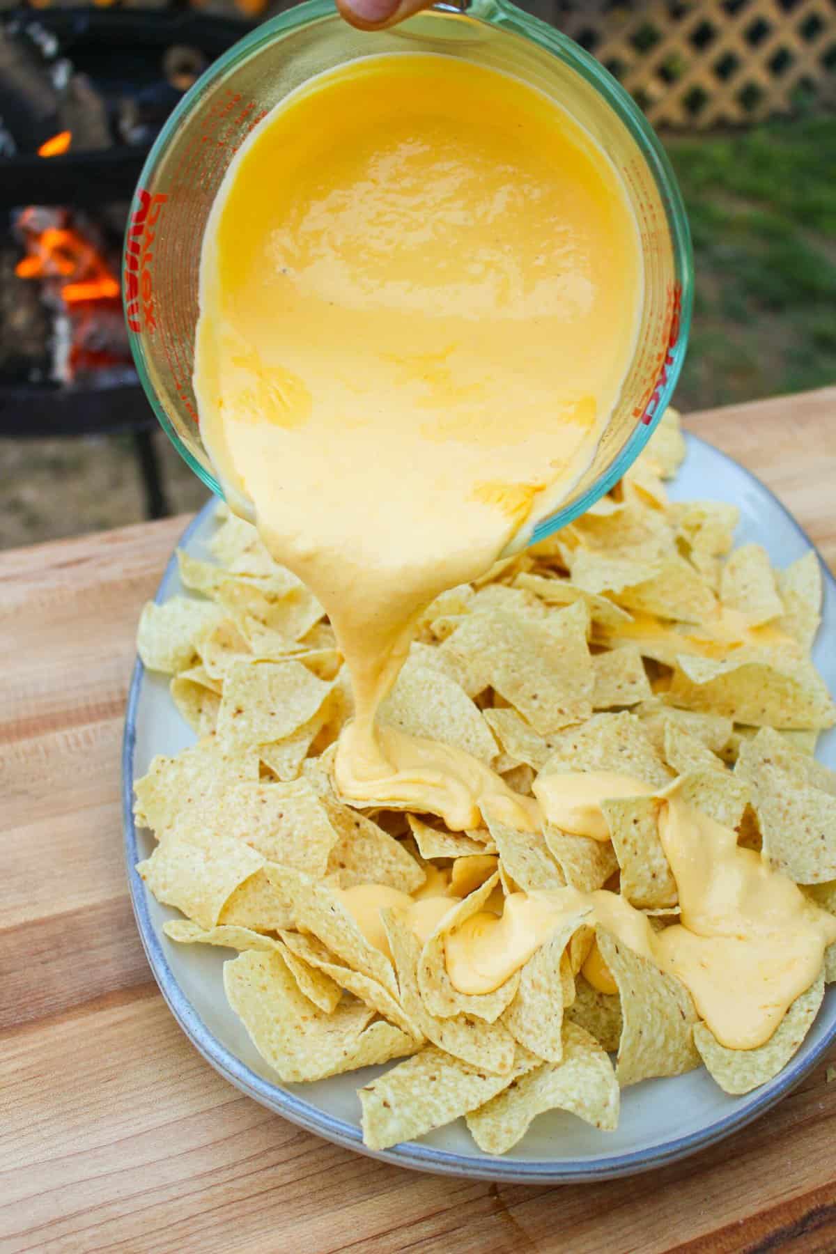 nacho cheese being drizzled over a platter full of tortilla chips