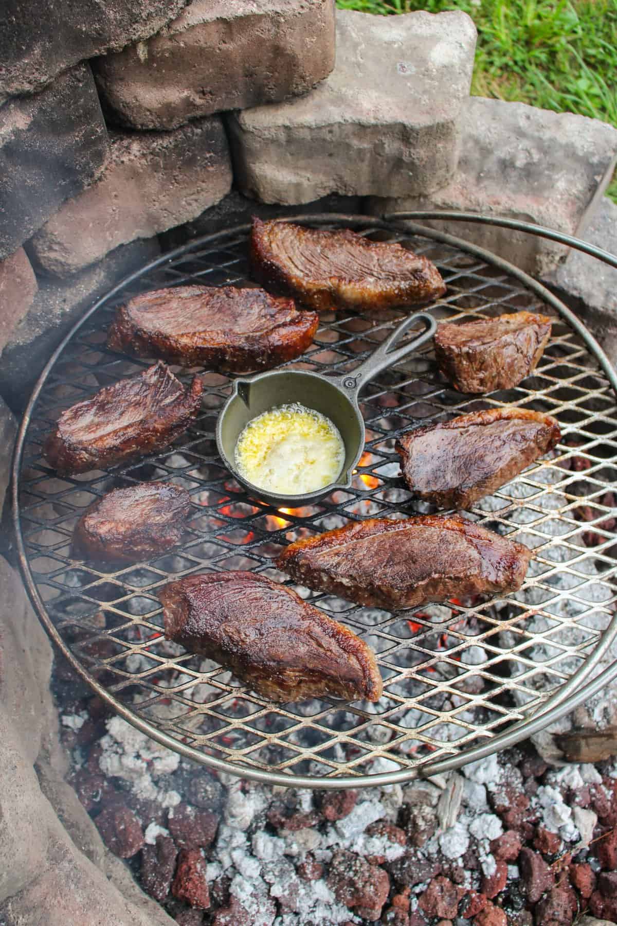 cooked pieces of steak surrounding a skillet with garlic butter on the grill