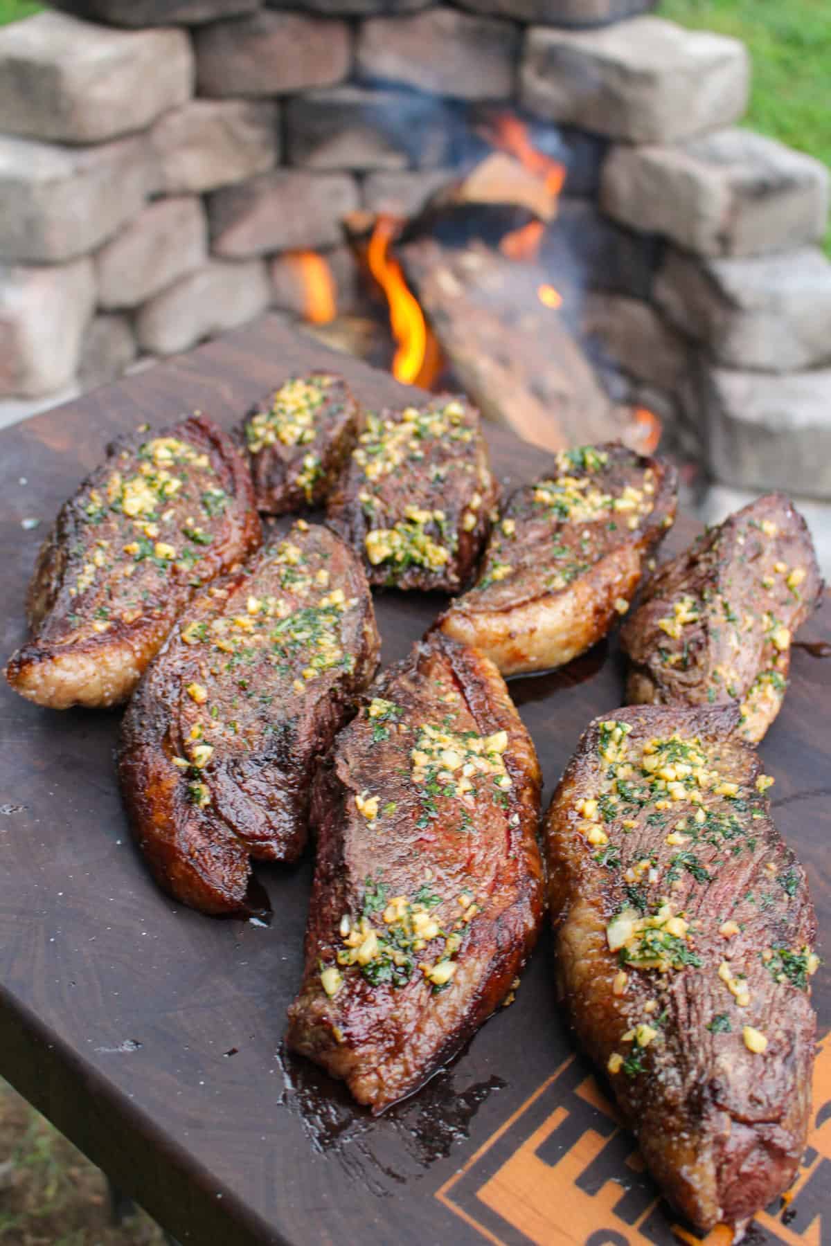 grilled picanha topped with garlic butter held next to a fire pit