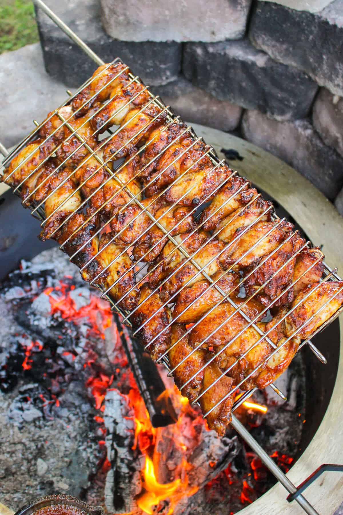 closeup of a rotisserie basket with chicken wings over a fire