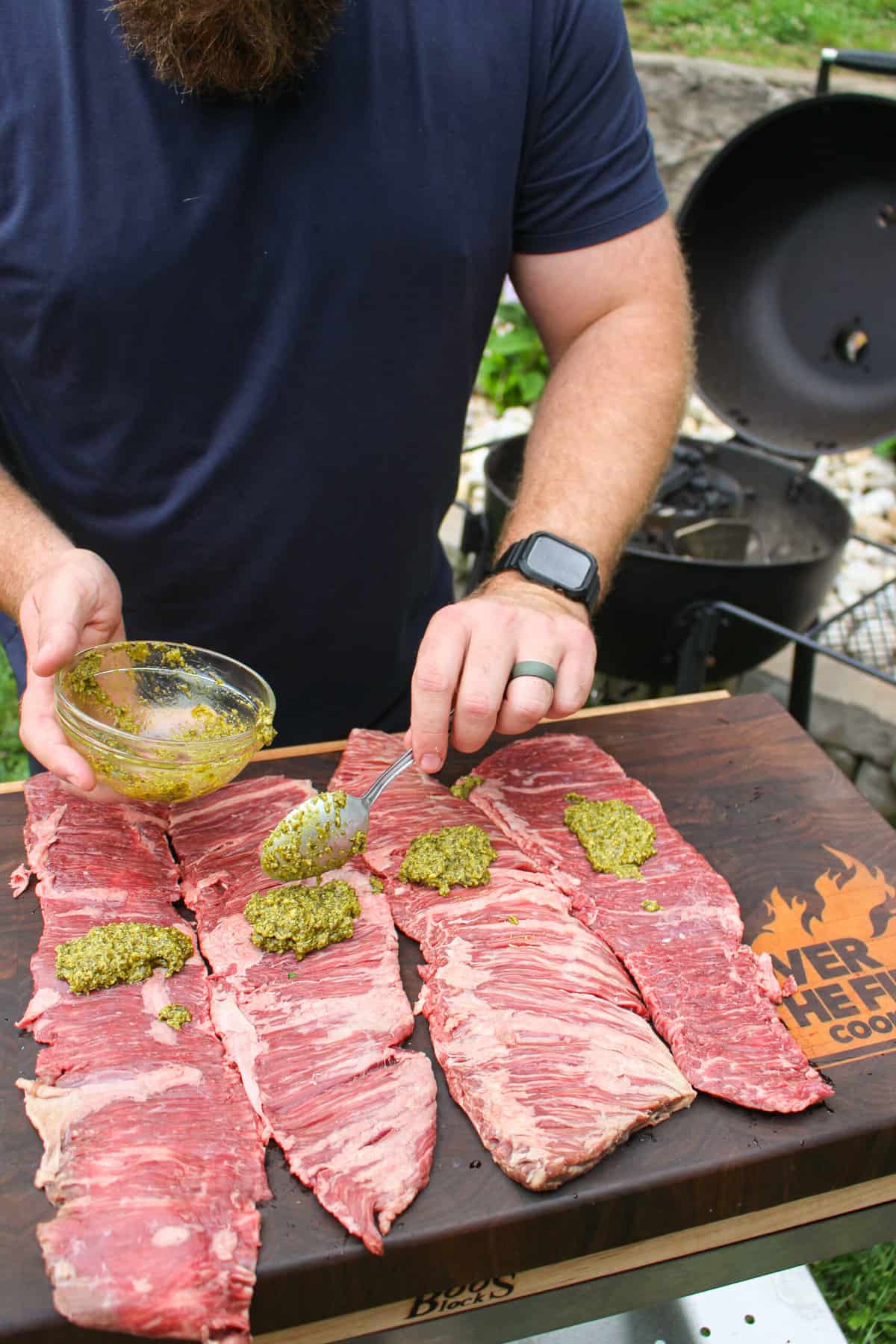 skirt steak being topped with spoonfuls of pesto