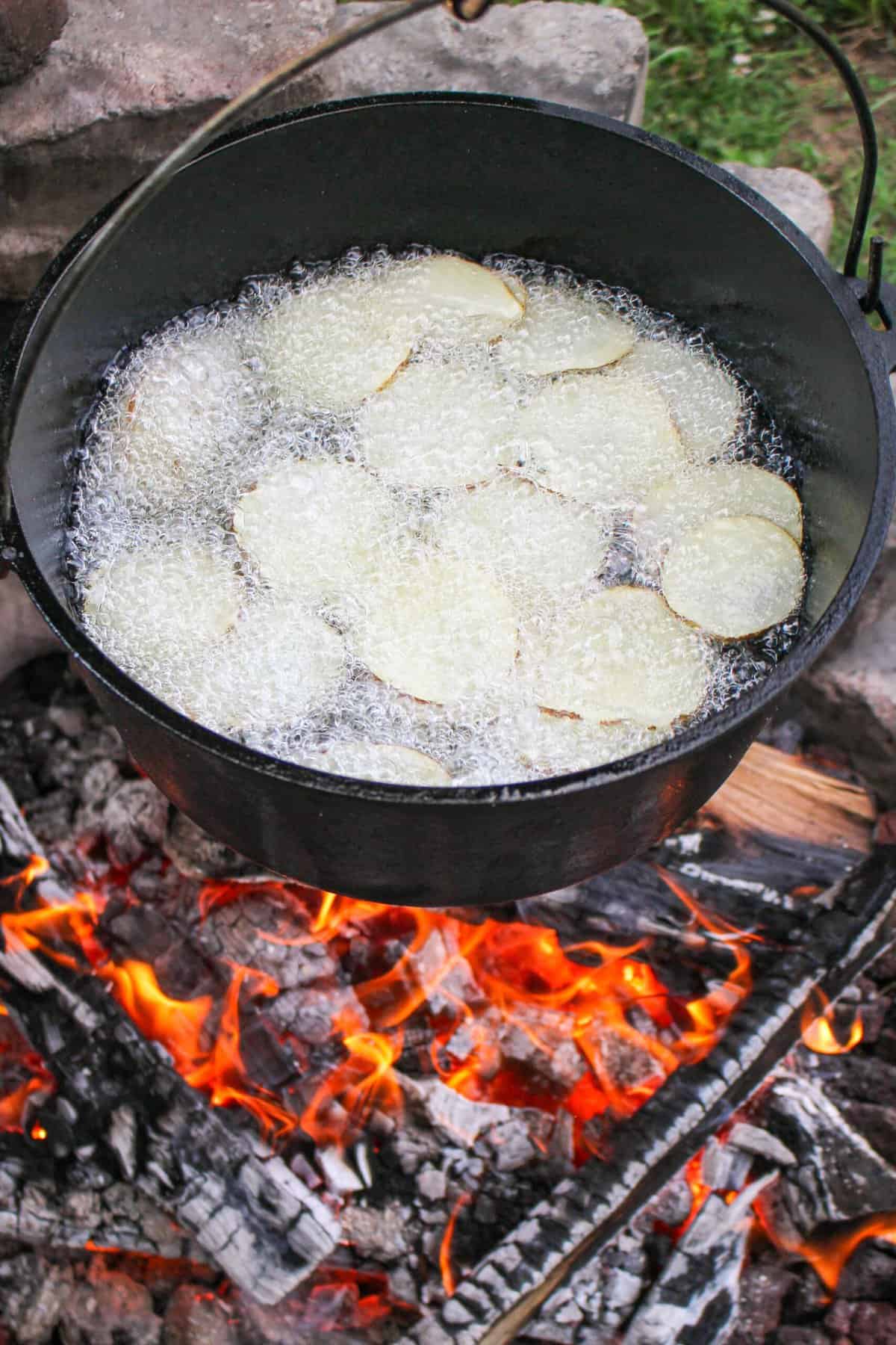 thinly sliced potatoes added to hot oil in a pot