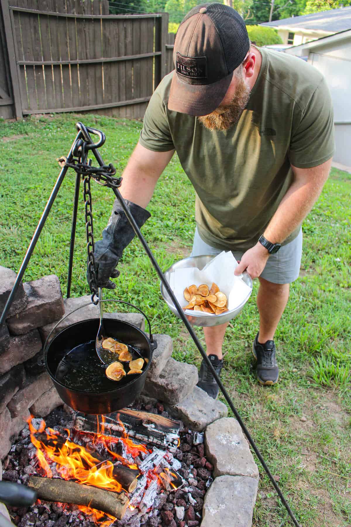 man standing over a fire pulling kettle chips out of a pan