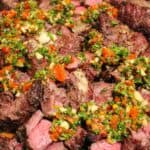 closeup of a pile of cubed steak topped with tomato herb chimichurri