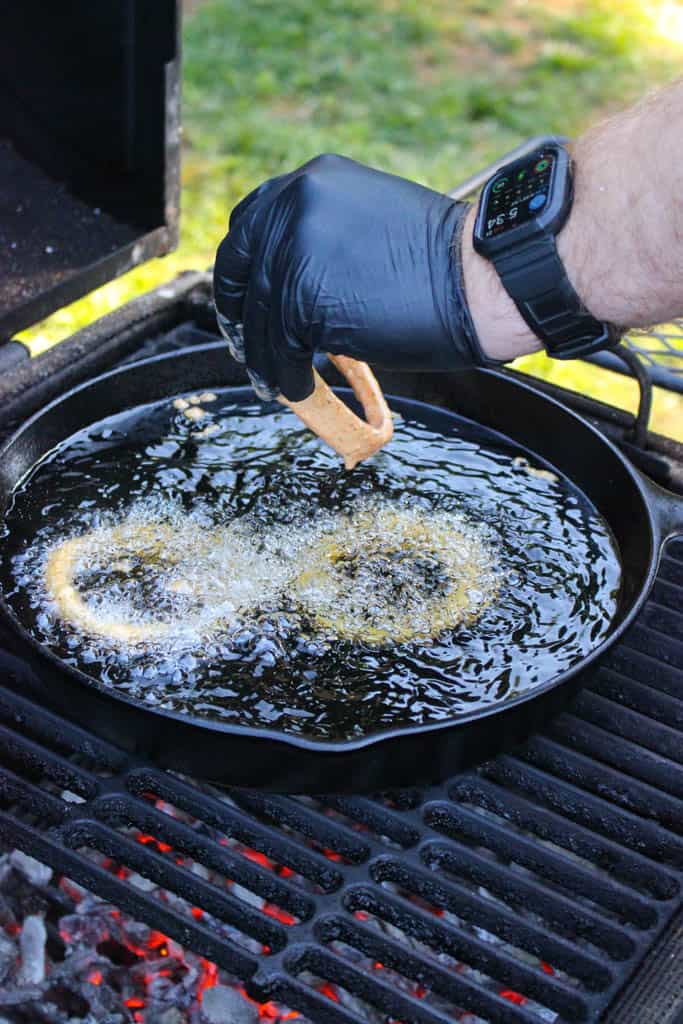 breaded onion rings being added to a skillet full of hot oil