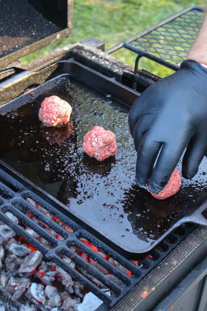 ground beef balls being added to a hot skillet pan on a grill
