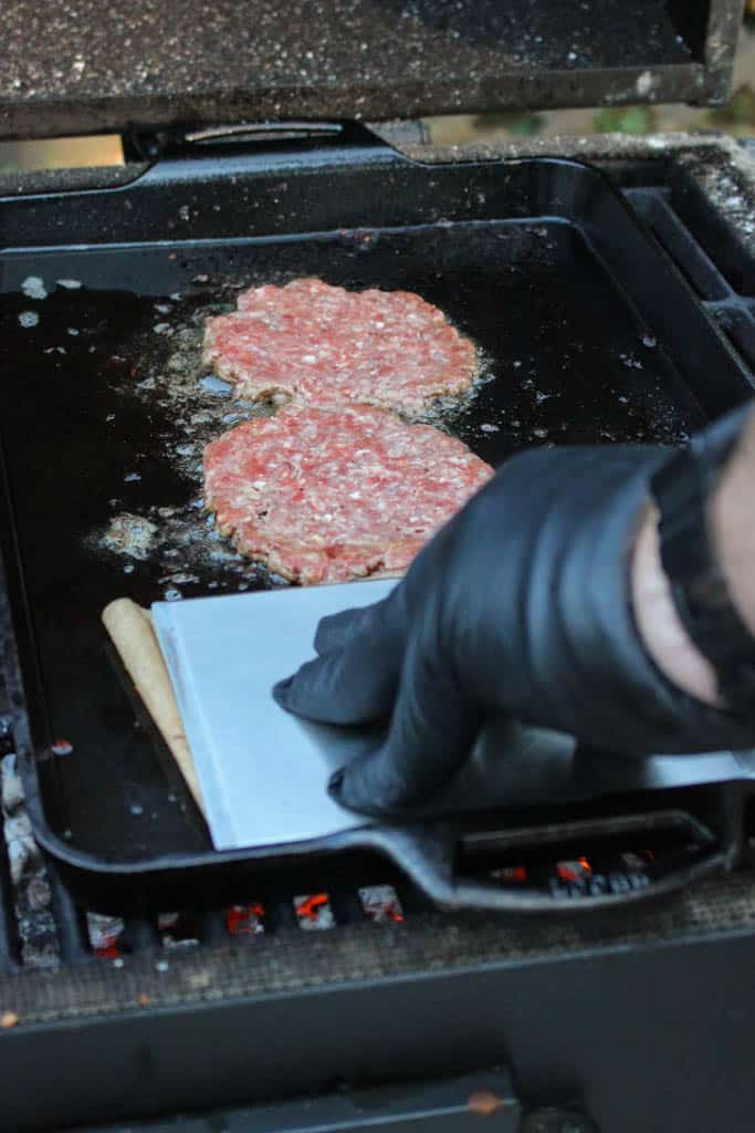 beef balls being pressed into patties using parchment paper and a spatula