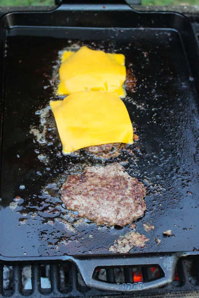 burger patties on a hot skillet topped with slices of cheddar cheese