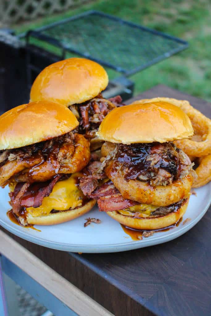 three fully assembled western bbq burgers on a plate with onion rings