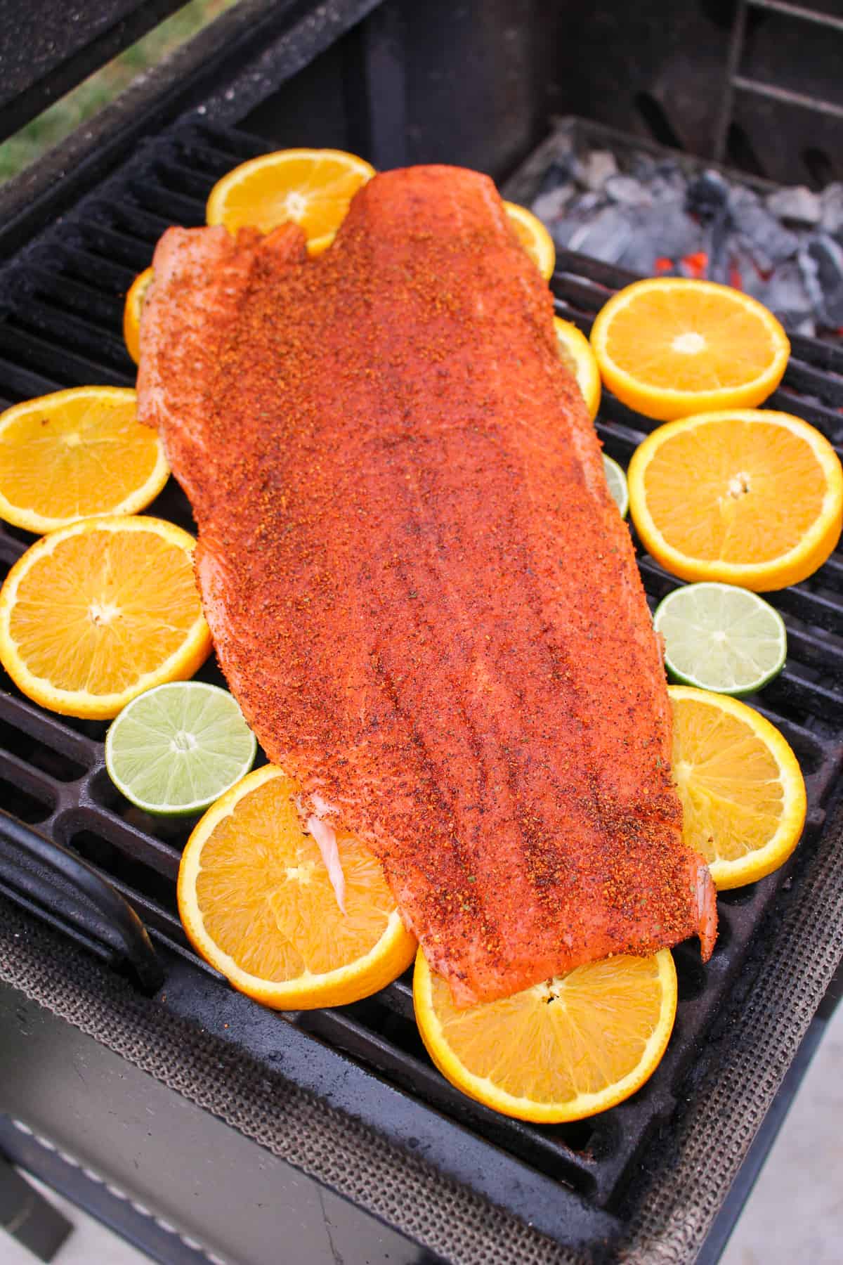 overhead of seasoned salmon on a "plank" of orange and lime slices on the grill