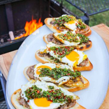 overhead of a plate lined with open faced cheese stuffed sausage sandwiches on a plate by a grill