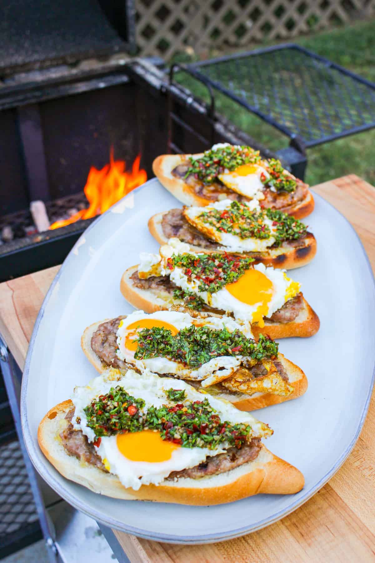 overhead of a plate lined with open faced cheese stuffed sausage sandwiches on a plate by a grill