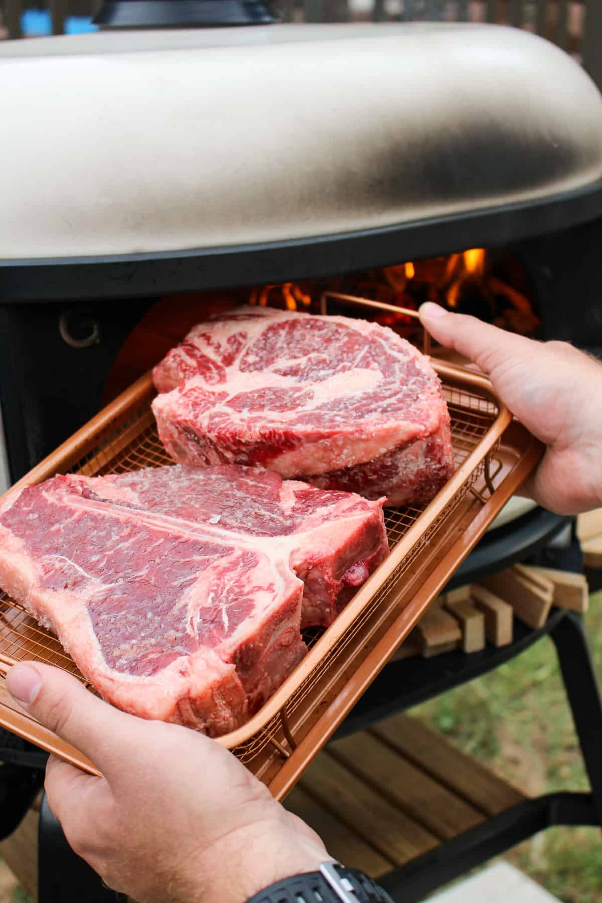 two steaks in a wire basket held by a pizza oven