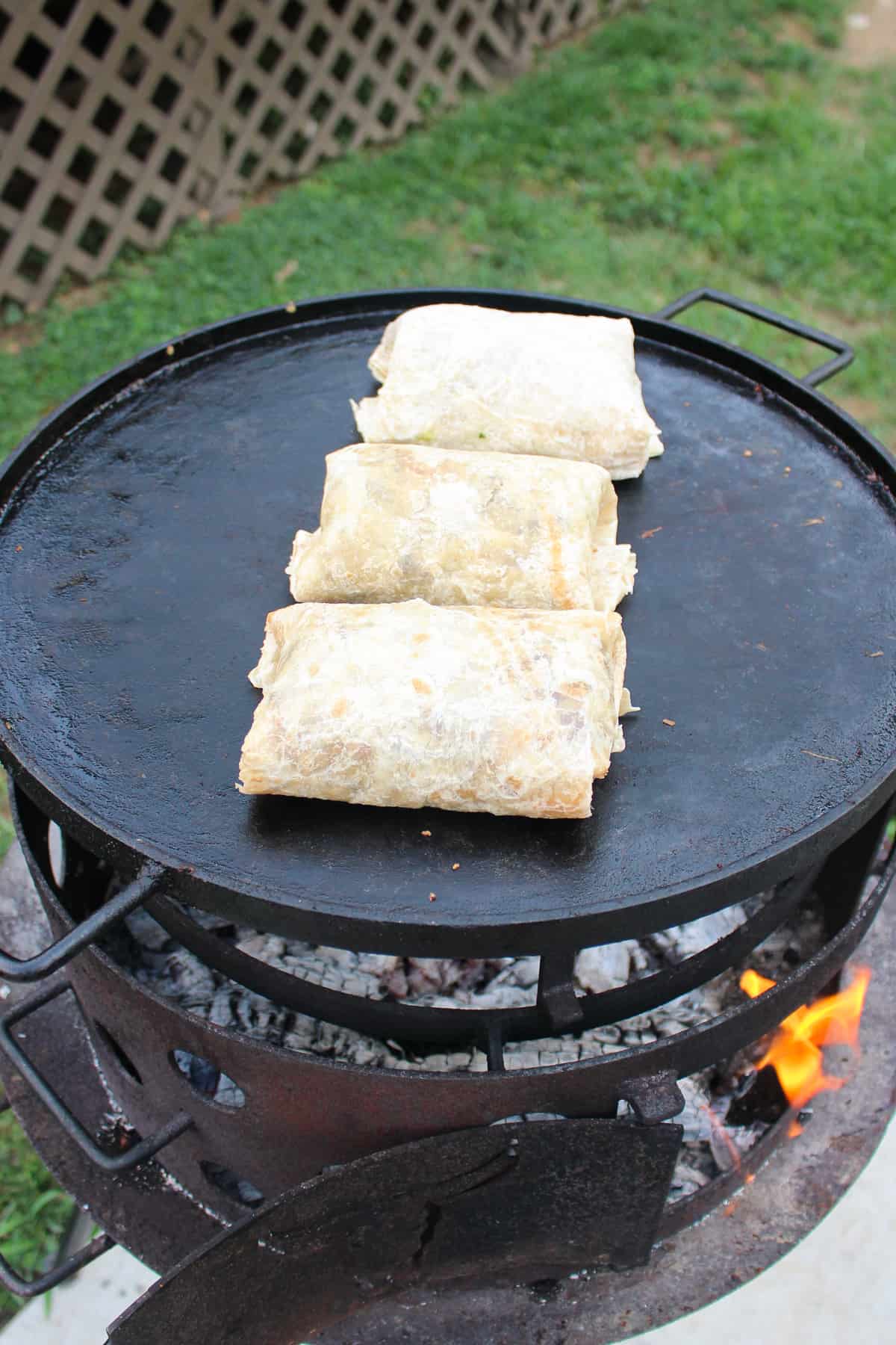 overhead of assembled chorizo breakfast burritos being crisped on a plancha