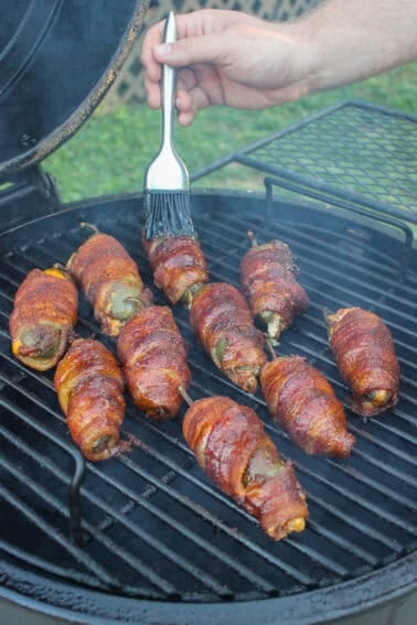 Glazing the smoked bacon wrapped jalapeños so they can caramelize before serving.