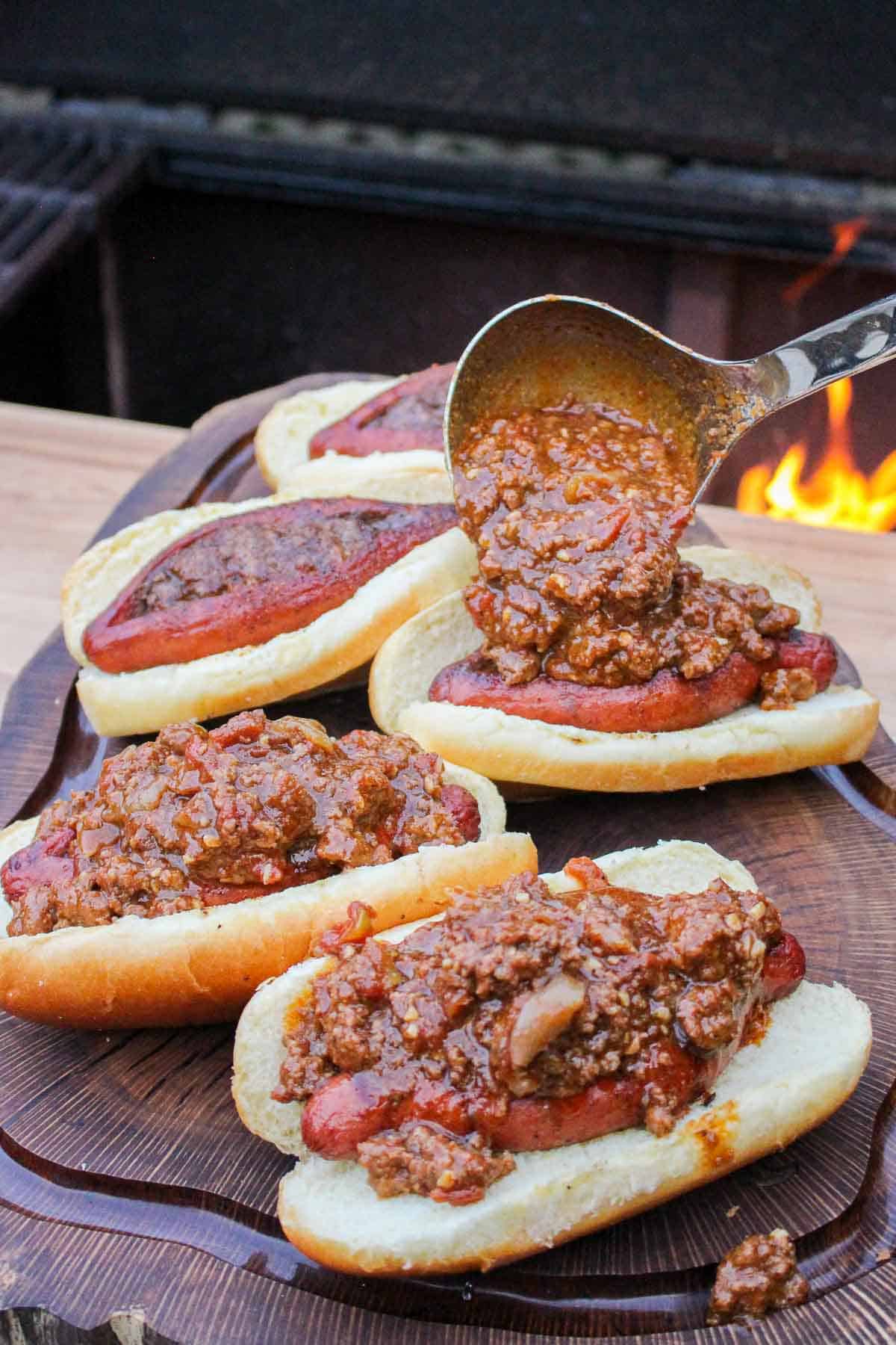 hot dog buns topped with hot dogs being ladled with chili