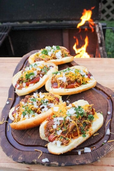 five chili cheese glizzburgers on a cutting board by a fire