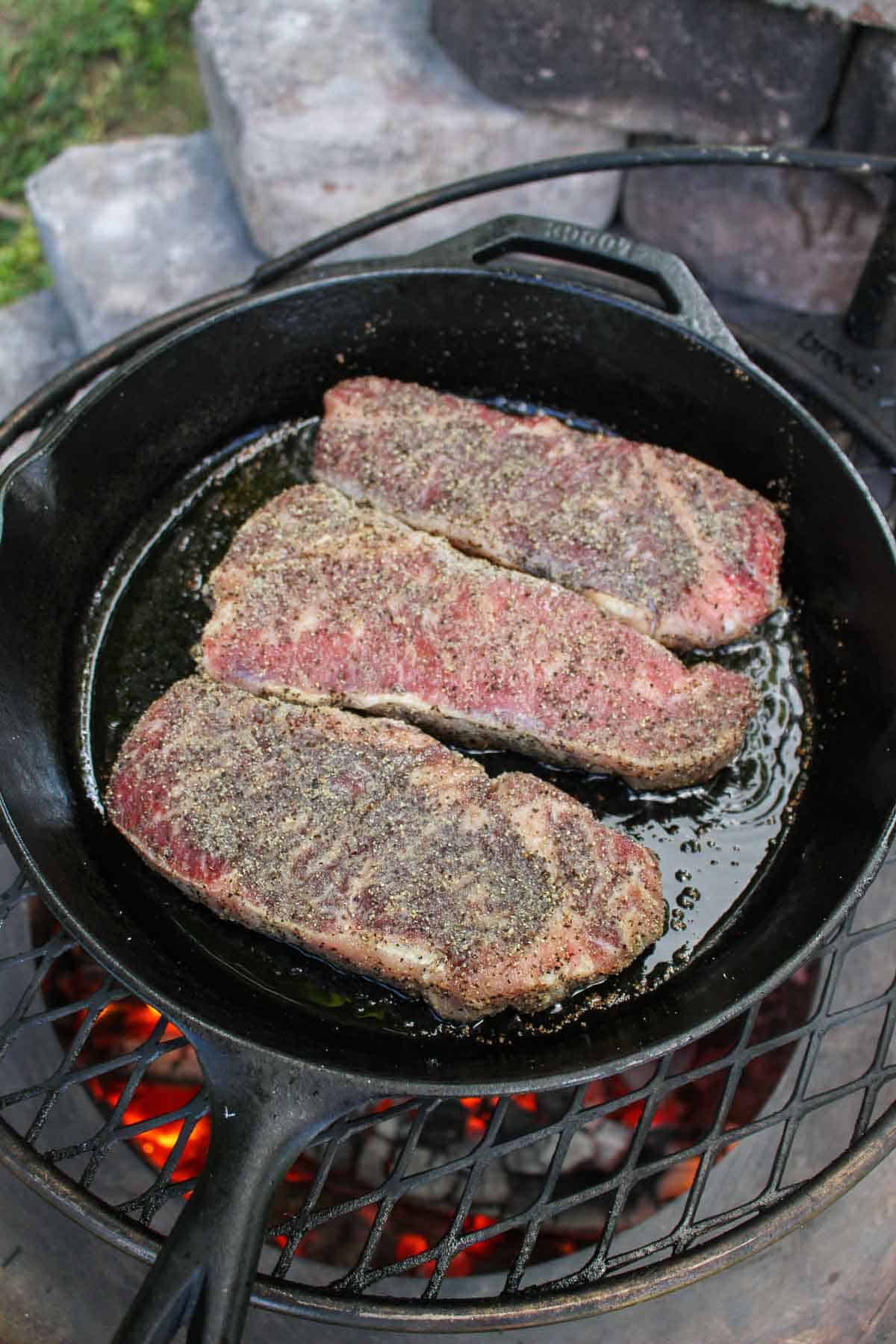 three strip steaks being cooked in a cast iron skillet