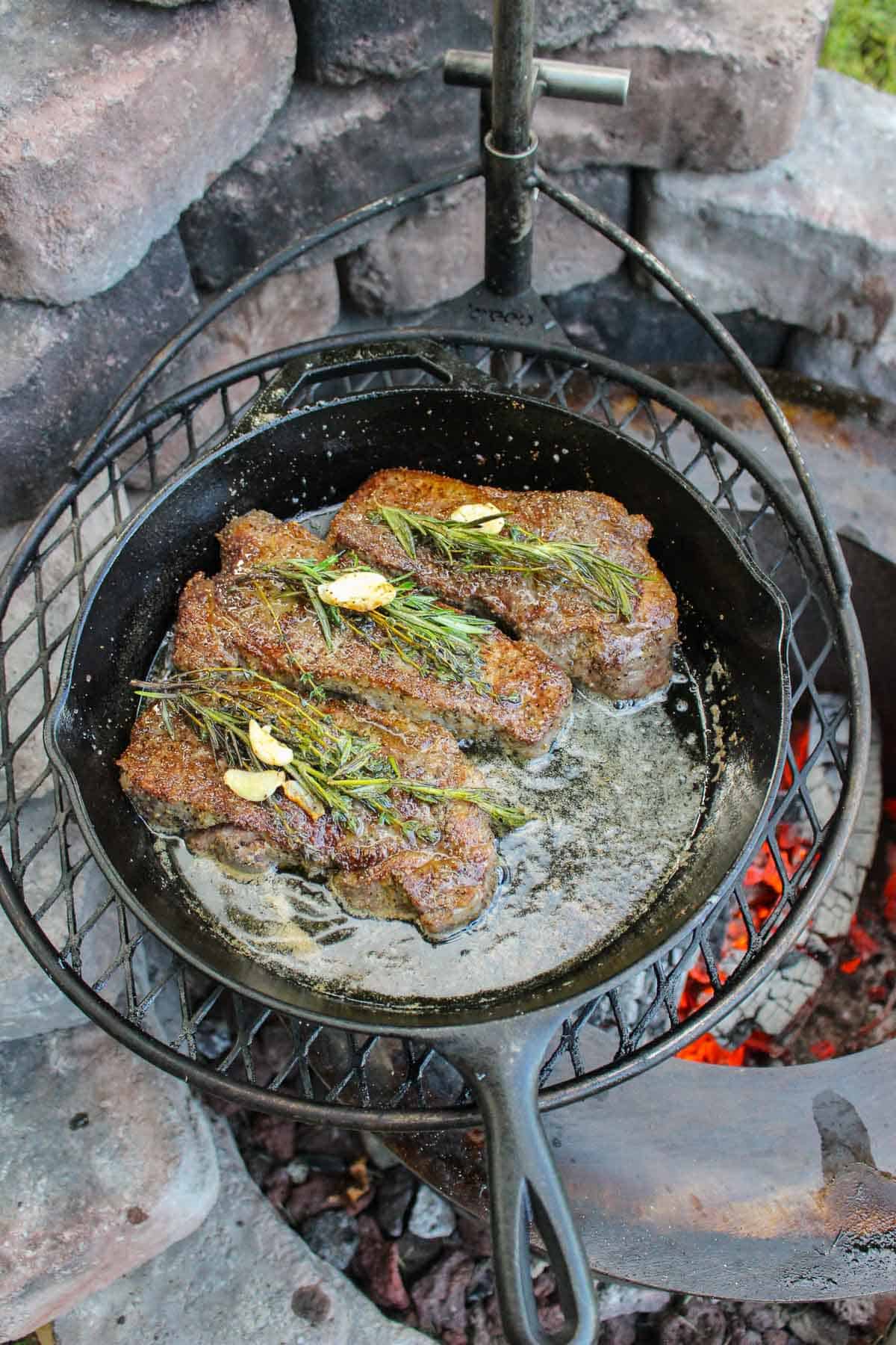 cooked strip steaks topped with garlic and fresh herbs in a skillet