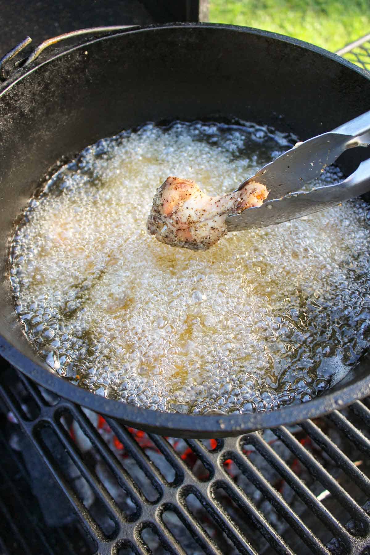 a chicken wing being placed into a pot of bubbling oil