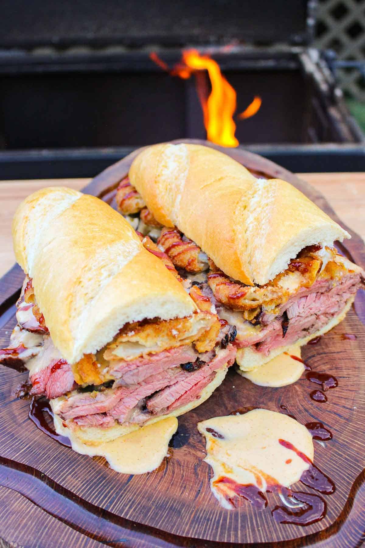 two halves of a bbq steak sandwich on a cutting board next to a grill