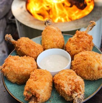 a plate filled with jalapeño chicken drumstick poppers with ranch next to a fire