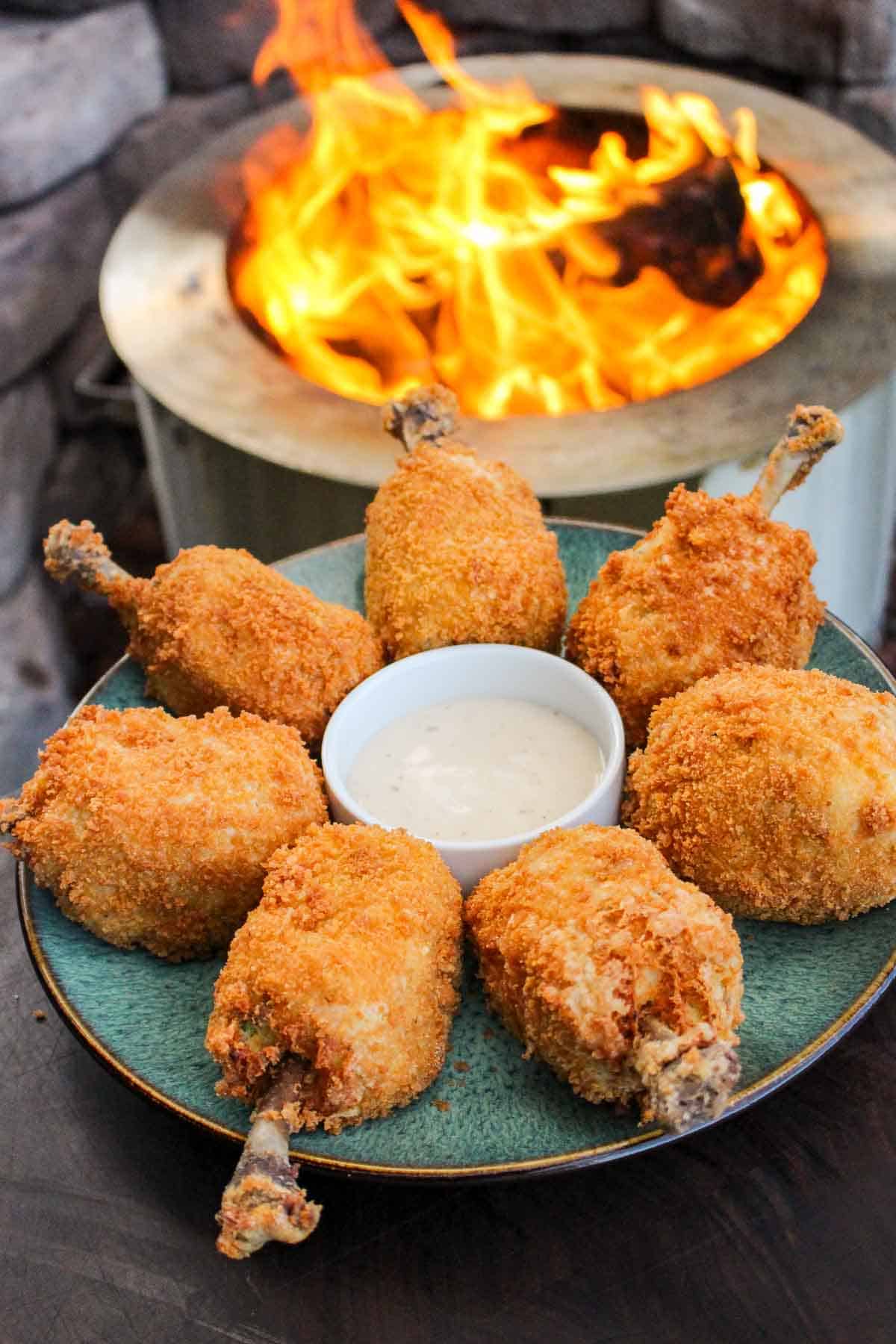 a plate filled with jalapeño chicken drumstick poppers with ranch next to a fire