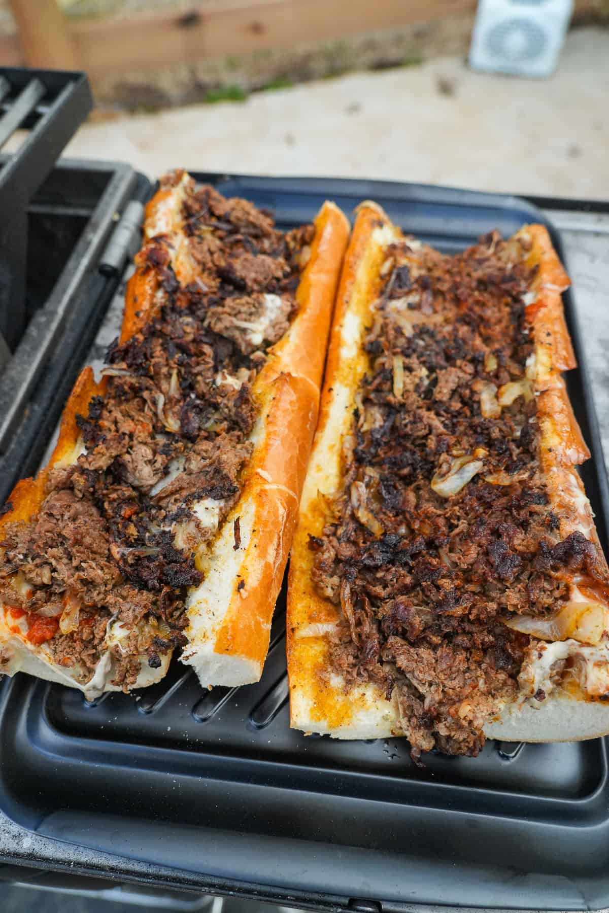 Assembling the sandwiches on the grill, with thinly sliced ribeye on top of the sandwich buns