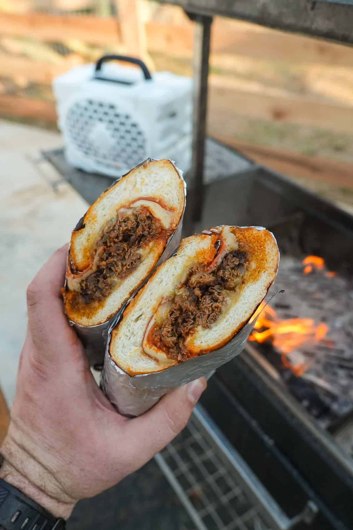 Derek Wolf holding up the sliced open pizza cheesesteak sandwich with a Turtlebox speaker in the background