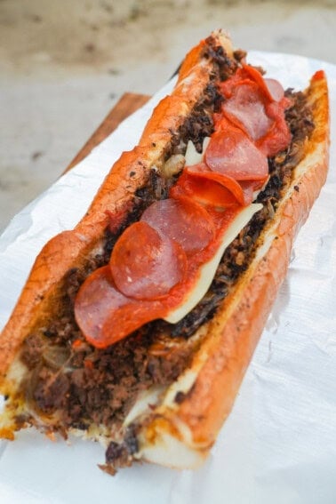 A fully assembled pizza cheesesteak sandwich, with pepperoni and cheese on top of thinly sliced ribeye