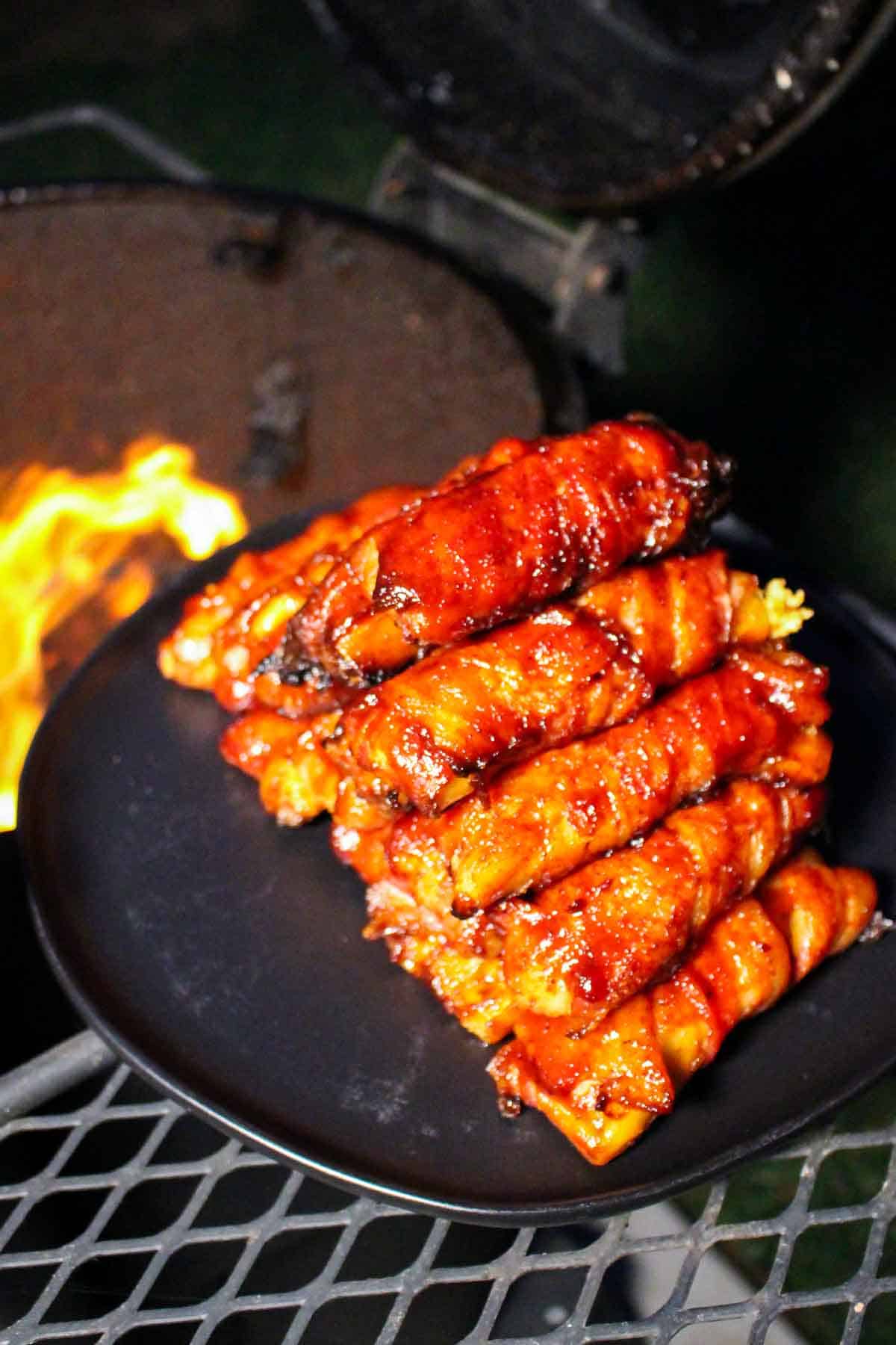 a stack of bacon wrapped manicotti shells on a plate by a smoker